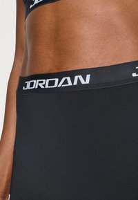 Μαύρη αθλητική μέση με σταθερή υφή, επενδυμένη με το λογότυπο "JORDAN" σε λευκά γράμματα, προσφέροντας υψηλή ελαστικότητα και άνε ση.