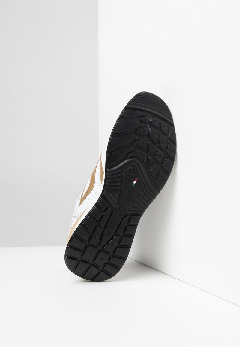 Sneaker bianca con accenti marroni, dotata di una suola in gomma nera testurizzata e dettagli del logo sul lato e sulla suola. Design atletico moderno.