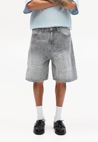 Shorts di denim grigi con motivi profondi, vestibilità rilassata, design a cinque tasche e chiusura con bottone. Abbinati a scarpe nere e calzini bianchi.