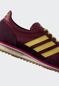 Bordová teniska Adidas so žltými pruhmi, béžovou podrážkou, ružovým akcentom, textúrovaným jazykom a logom adidas na pätnej časti aj podrážke.