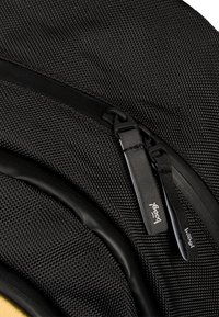 Zaino in tessuto nero con texture, con accenti neri lisci, che presenta una cerniera prominente e un'etichetta del marchio discretamente cucita sul lato.