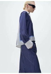 Completo a righe blu navy composto da giacca ampia con rifiniture in azzurro chiaro a contrasto e pantaloni a gamba larga, realizzati con una vestibilità rilassata.