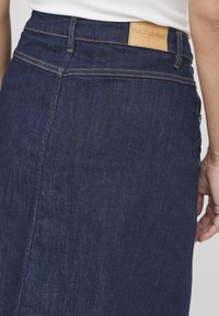 Mörkblå denimkjol med rak passform, med stickningsdetaljer och en läderetikett som säger "PULZ JEANS" på bakre midjan.