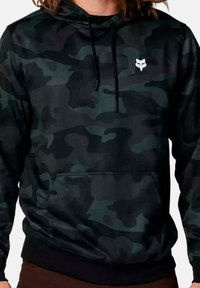 Sudadera con capucha de camuflaje en negro y verde, con cordón en la capucha, bolsillo frontal y logo blanco en el pecho. La tela parece suave con un ajuste informal.