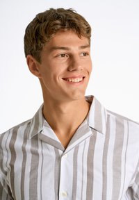 Camisa de manga corta con cuello, con rayas alternas en blanco y marrón claro, confeccionada en tela ligera. Presenta un corte relajado y cierre de botones.