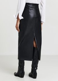 Jupe midi en cuir noir à taille haute avec une fente au dos, associée à des bottes noires montantes jusqu'au genou. Texture lisse et design élégant.