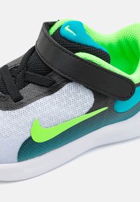 Nike Sneaker mit einem weißen Mesh-Obermaterial und schwarzen Akzenten, lebhaften grünen und blauen Details sowie einem schwarzen Klettverschluss.