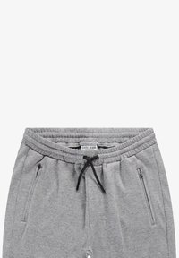 Grijze sweatpants van textuurstof met een tailleband met trekkoord, met twee ritszakken aan de zijkant. Merkenlabel zichtbaar aan de bovenkant.