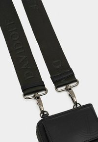 Schwarze Lederhülle mit glatter Oberfläche, ausgestattet mit einem Reißverschluss und einem geprägten Logo. Befestigt sind zwei verstellbare, dunkelgrüne Riemen mit eleganten Metallclips.