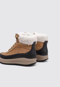 Braune Wildlederschuhe und schwarze Leder-Stiefeletten mit weißem Pelzfutter, runden Schnürsenkeln, goldenen Beschlägen und dicken beige Gummisohlen.