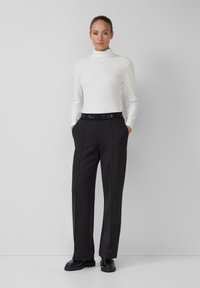 Pull en col roulé blanc à côtes et pantalon noir taille haute avec ceinture de marque noire ; texture lisse et design à jambes larges ; chaussures noires brillantes.