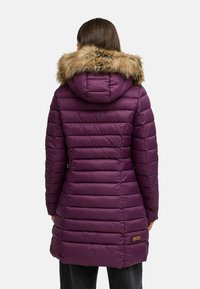 Chaqueta acolchada púrpura con capucha de piel sintética, diseño de acolchado vertical y bolsillos laterales. Presenta una pequeña etiqueta de logo cerca del dobladillo.