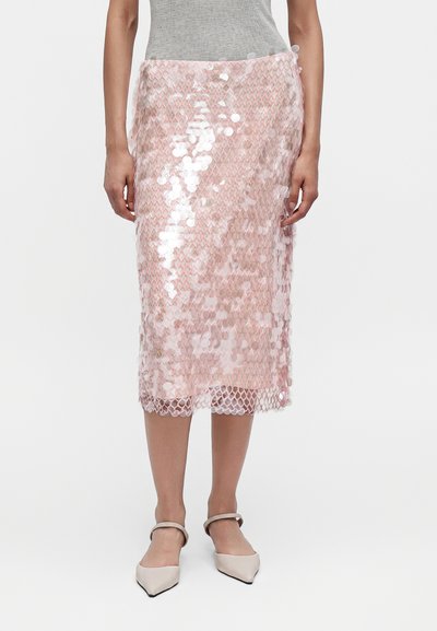 Femme portant une jupe midi rose à sequins associée à un top gris sans manches et des chaussures beige à bout pointu et bride à la cheville.