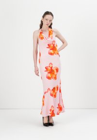 Rosa halterneck kjole med livlig oransje blomstermønster, tettsittende silhuett og flagrende kant, kombinert med svarte høyhælte sko.