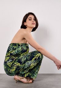 Mono sin tirantes con fondo azul marino y patrones de hojas tropicales en verde y amarillo. Combinado con sandalias doradas de tiras, que realzan una cintura ceñida.