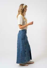 Haut léger à manches courtes, associé à une longue jupe en jean bleu avec des boutons et une fente sur le côté, complété par des baskets grises.