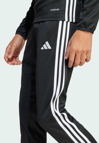 Svarta träningsbyxor i slät tyg med vita tre-stripes detaljer längs sidorna och en Adidas-logotyp. Inkluderar en Aeroready-logotyp.