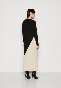 Stickad klänning med en svart överdel och en beige underdel med en diagonal söm. Den har långa ärmar, en rund halsringning och en figurnära silhuett.