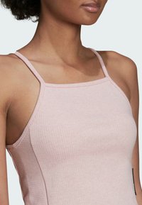 Camiseta de tirantes delgados en color rosa claro, con un escote cuadrado, que presenta una textura sutil y una pequeña etiqueta de logo en el lado.