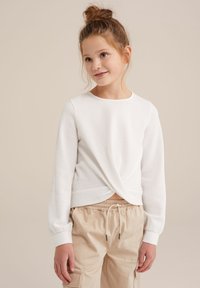 Vit långärmad topp i strukturerad trikå med en framvikt detalj och rund halsringning, kombinerad med beige byxor med dragsko.