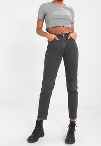 Černé džíny s vysokým pasem a slim fit, zkrácený šedý ribbovaný top s vlnitou spodní částí a černé šněrovací boty. Hladká textura.