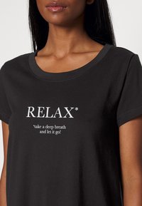Čierne bavlnené tričko s okrúhlym výstrihom, krátkymi rukávmi a veľkým bielym nápisom "RELAX*" s menšou frázou pod ním.