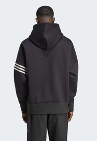 Sudadera negra con una capucha grande, tres franjas blancas en la manga izquierda y un dobladillo ajustado en la parte inferior. Textura de tela suave, ajuste relajado.