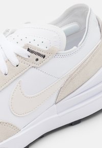 Nike tenisice s gornjim dijelom od bijele kože, bež nubuk detaljima, bijelim vezicama i teksturiranim đonom. Uključuje perforirane detalje na prstima.