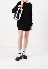 Czarna dzianinowa sukienka w prążki z długimi rękawami, połączona z czarno-kremową torbą, białymi skarpetkami i masywnymi czarnymi butami.