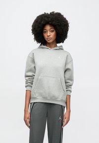 Hall halliga kapuutsiga dressipluus kängurutaskuga, millel on väike valge Jordani logo. Sobitatuna tumedate hallide dressipükstega, mille külgedel on triibud.