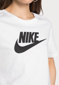 Camiseta de algodón blanca con un gran logo de Nike en negro y el gráfico del swoosh en el frente. Diseño clásico de cuello redondo, manga corta.