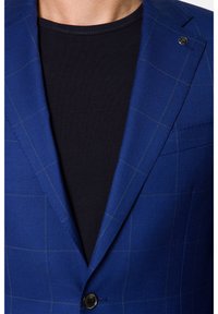 Niebieska marynarka w kratę o gładkiej fakturze, z pojedynczym zapięciem na guzik i klapami w kształcie notcha, noszona na czarnej koszulce z okrągłym dekoltem.