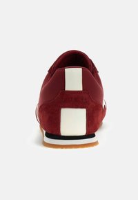 Bordeauxfarbener Sneaker mit einer strukturierten Oberseite aus Wildleder und Synthetik, weißen Akzentstreifen, einer Gummisohle und einem gepolsterten Schaft für Komfort.