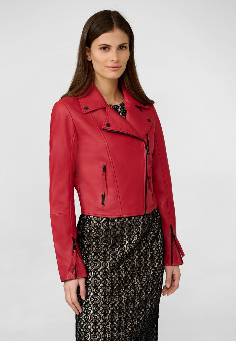Veste de moto courte en cuir rouge avec une fermeture éclair à l'avant, col à revers et quincaillerie noire ; associée à une robe en dentelle noire.