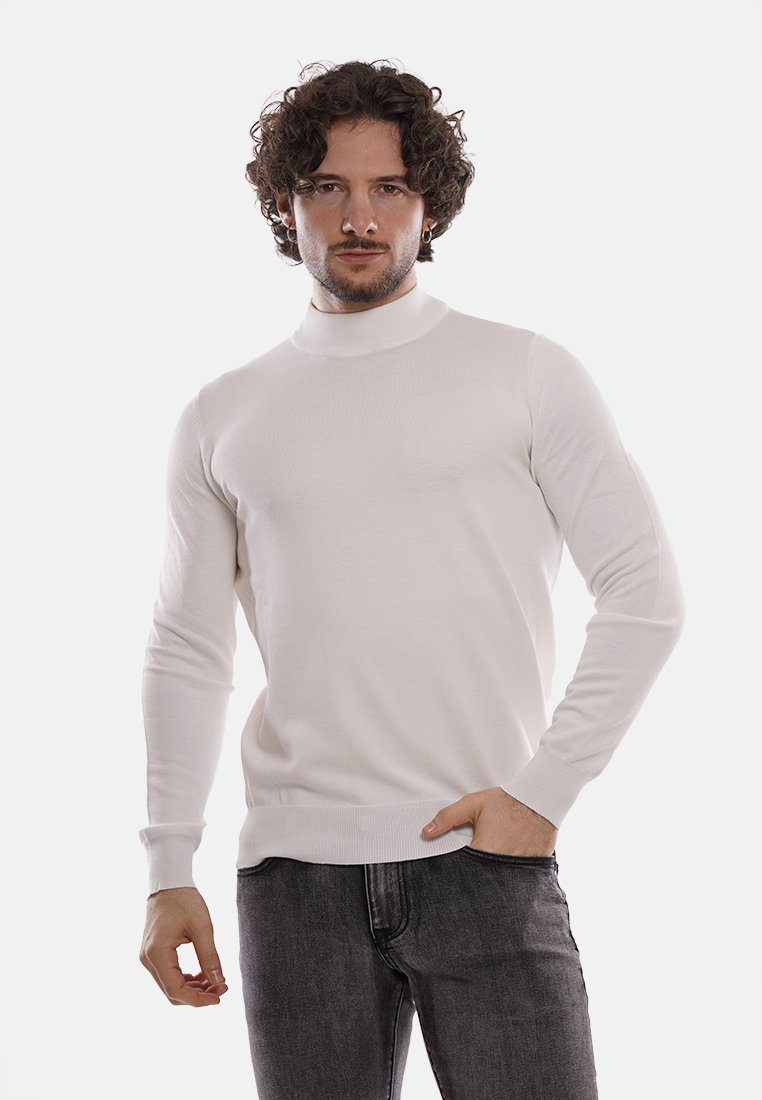 Maglione bianco attillato a collo alto con una superficie liscia, maniche lunghe e polsini a coste. Indossato con jeans in denim scuro.