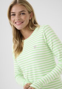 Camicia a maniche lunghe bianca con righe verdi, con un piccolo emblema a forma di cuore. Tessuto di cotone morbido con scollatura rotonda.