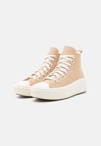 Beżowe sneakersy typu high-top z gładkiej skórzanej cholewki, białym gumowym noskiem i podwyższoną białą platformą. Posiadają metalowe oczka i płaskie sznurowadła.