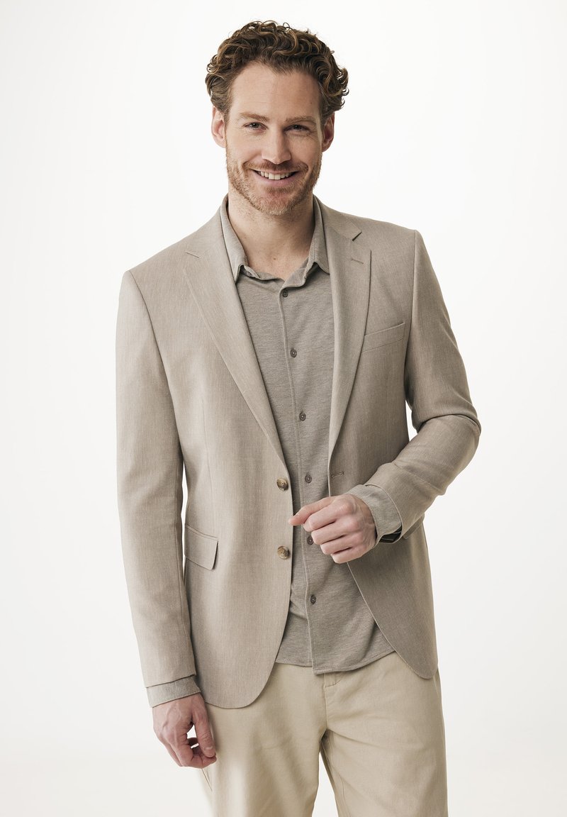 Světle béžový blazer s přiléhavým střihem, jednoduše zapínaný, se dvěma knoflíky. Nositelný přes šedou košili, v kombinaci se světlými kalhotami.