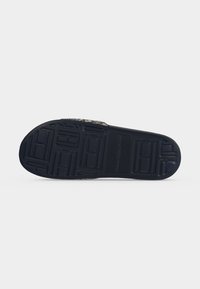 Semelle en caoutchouc noir d'une chaussure à enfiler avec des motifs de sculpture géométriques et le logo Tommy Hilfiger embossé au centre.