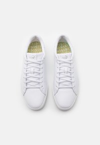 Vita sneakers med en slät läderöverdel, designade med sex hål för snörning och platta snören; grönmönstrad innersula med varumärkeslogotyp.