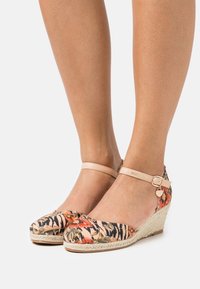 Alpargatas con cuña de patrón floral, con parte superior de tela en tonos de rosa, naranja y negro. Presentan una correa en el tobillo de color beige y suela de yute trenzado.