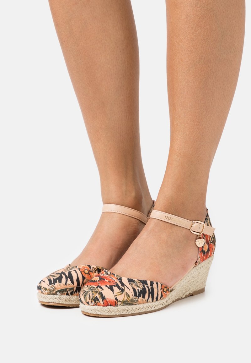Alpargatas con cuña de patrón floral, con parte superior de tela en tonos de rosa, naranja y negro. Presentan una correa en el tobillo de color beige y suela de yute trenzado.