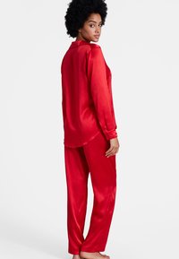 Ensemble de pyjama en satin rouge comprenant un haut à boutons avec un col et des manches longues, associé à un pantalon ample, mettant en valeur une texture lisse.