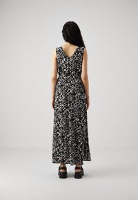 Robe à motif floral en noir et blanc avec un dos en V, sans manches, jupe fluide et taille ajustée. Associée à des sandales noires épaisses.