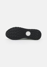 Black rubber shoe sole with circular traction pattern and a central hole design, featuring a slight curve at the heel edge for enhanced grip.