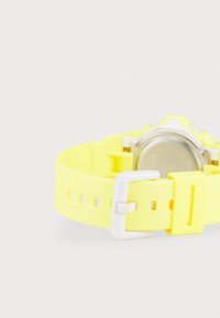 Yellow silicone watch strap with a white buckle, featuring cutouts for adjustability and a round metallic watch case on the back.