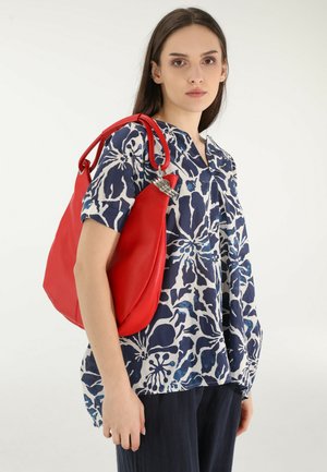 Rote Ledertasche mit strukturiertem Finish und silberfarbener Hardware, kombiniert mit einer navyblauen Bluse mit floralem Muster in Weiß.