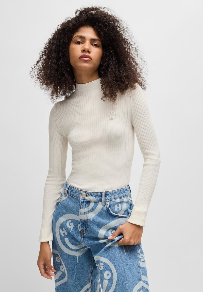 Ribbede, kremfargede langermede topp med høy hals. Kombinert med blå jeans med store hvite grafiske smilefjes.
