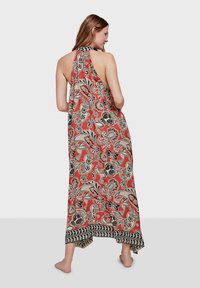 Vestido maxi de tela roja con patrón floral en negro y beige, diseño de cuello halter, espalda descubierta y dobladillo con patrón contrastante. Material ligero.