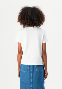T-shirt en coton blanc à manches courtes, col rond et coupe décontractée, associé à une jupe en denim bleue avec une fente à l'arrière.